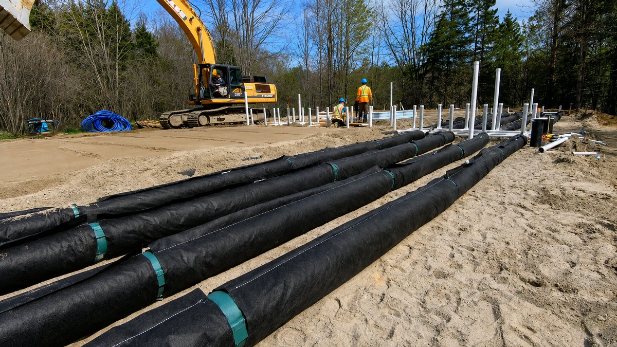 Treatment lines laid on a sand bed in woodland, with an excavator and field crew