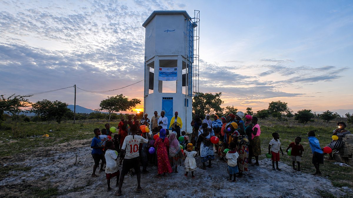 Residents and children with balloons gathered around a water tower being brought into service at sunset